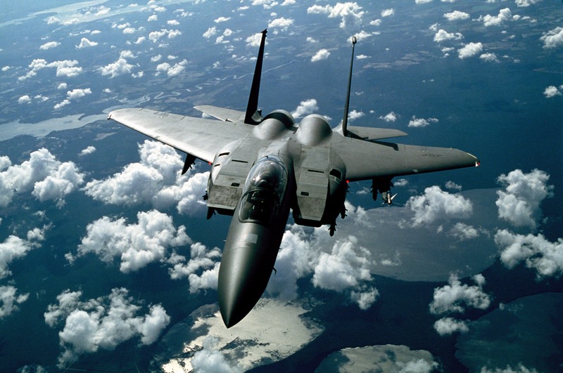 Colored photograph of dark gray  jet fighter F-15 strike eagle ,as appears in Aaron David Yeoman's political thriller novels,flying above the clouds